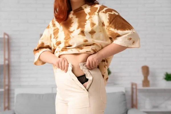 Image of woman trying to do her trousers up after pregnancy weight gain Marlborough